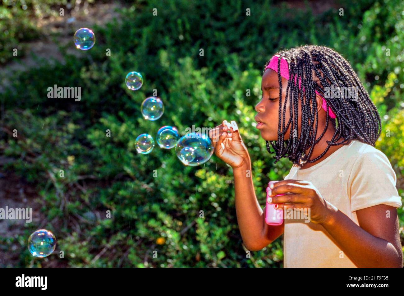 An African American girl blows bubbles in a suburban garden in Corona ...