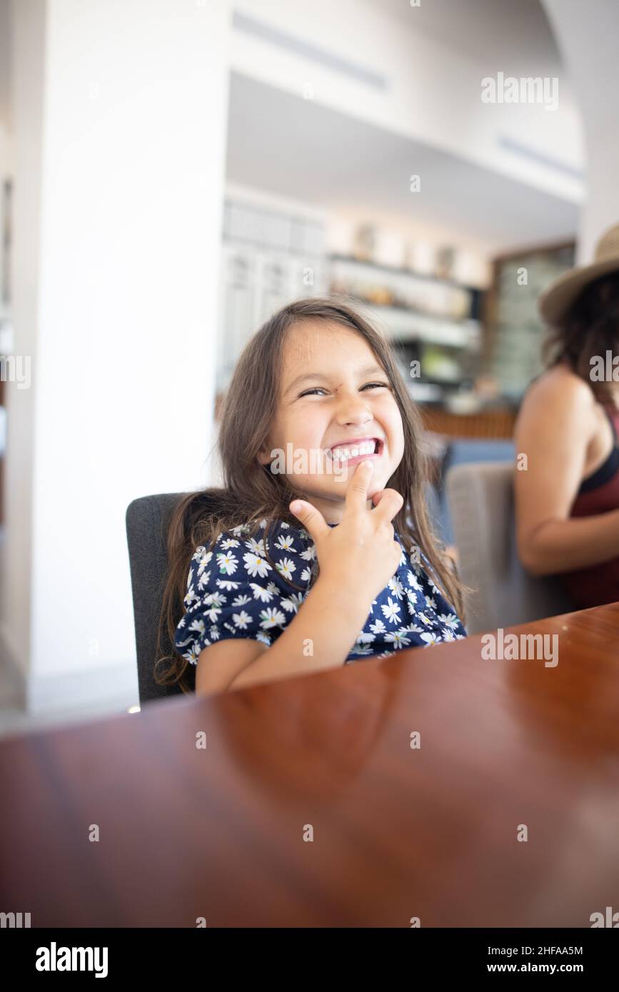 Cute little girl sitting at a restaurant table and smiling gracefully ...