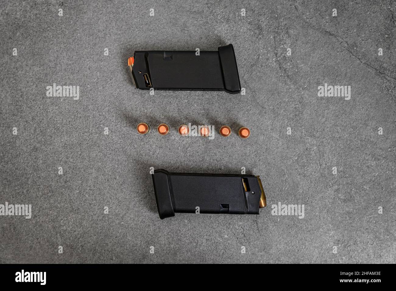 45 ACP caliber hollow point and full metal jacket bullets loaded into handgun magazines and unfired rounds lined up on a stone surface Stock Photo
