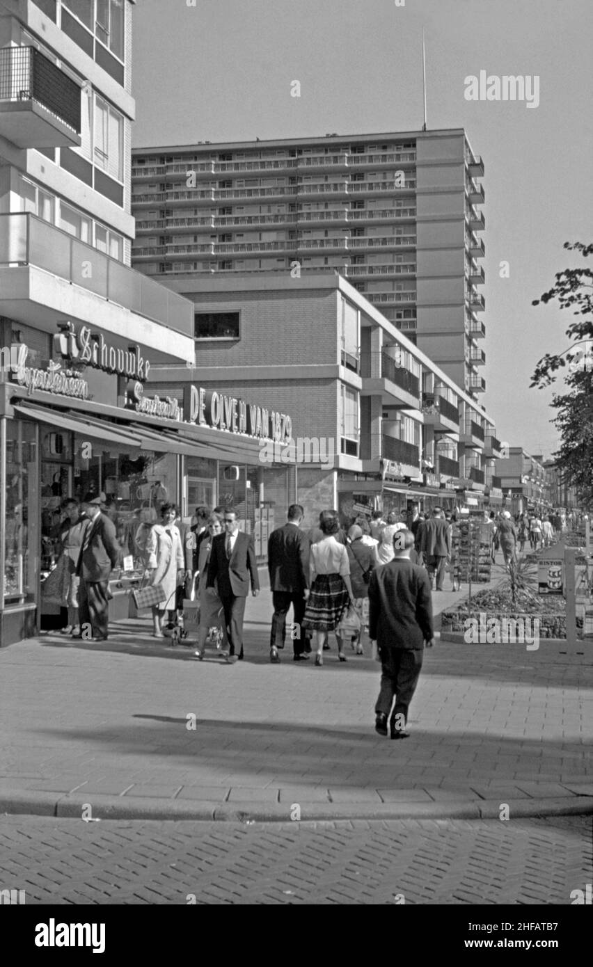 A view of shops at street level and apartment blocks along Karel Doormanstraat, the (de) Lijnbaan, Rotterdam, the Netherlands in the 1960s. The layout of the residential development, which opened in the late 1950s, separated shops from apartments and were arranged around green courtyards. It was designed by the firm Van den Broek & Bakema led by architects Jo van den Broek and Jacob B (Jaap) Bakema. Today this area completely pedestrianised with many eating and drinking places with outdoor seating along this street – a vintage 1960s photograph. Stock Photo