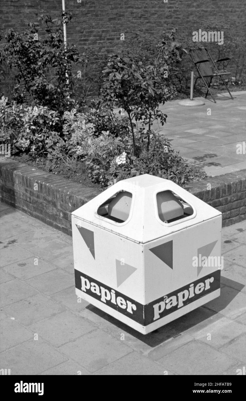 A collection bin for recycling paper at the (de) Lijnbaan, Rotterdam, the Netherlands in the 1960s. This stylish, environmentally-friendly receptacle would have been a rare sight at that time but is very common today. The Lijnbaan is the main shopping precinct of Rotterdam. It was opened in 1953. It was the first purpose-built pedestrian street in Europe. Flower beds, benches and protective canopies were provided. The car-free area proved successful and has influenced similar schemes worldwide. This image is from an old amateur black and white transparency – a vintage 1950s/1960s photograph. Stock Photo