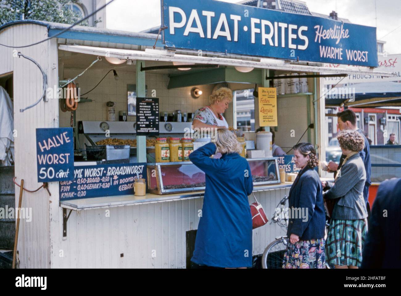 A fast food, takeaway market stall selling delicious (‘heerlijke’) sausage and chips (worst and patat) in the centre of Apeldoorn, Gelderland, the Netherlands c. 1960. This image is from an amateur Kodak 35mm colour transparency – a vintage 1950s/1960s photograph. Stock Photo