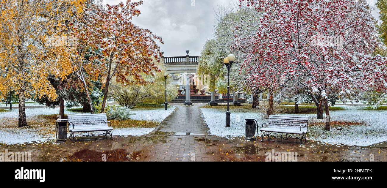 Cozy corner of autumn city park after first snowfall - late autumn or early winter landscape. Colorful fall foliage, red berries of rowan and wild app Stock Photo