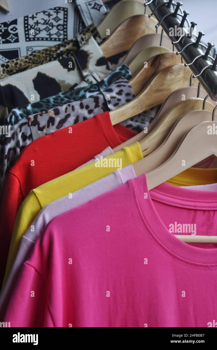Multicolored t-shirts and shirts hanging on hangers in shop for sale - Stock Photo Stock Photo