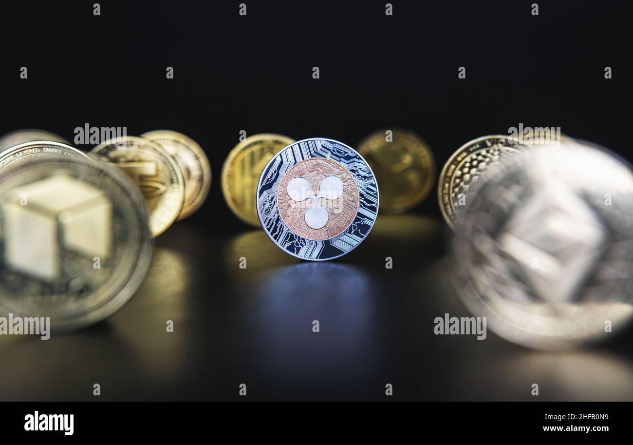 Ripple XRP next to many cryptocurrency coins like defocused Ethereum, Neo, Tether on black background. Central composition, low key photo for banners and news about crypto. Stock Photo