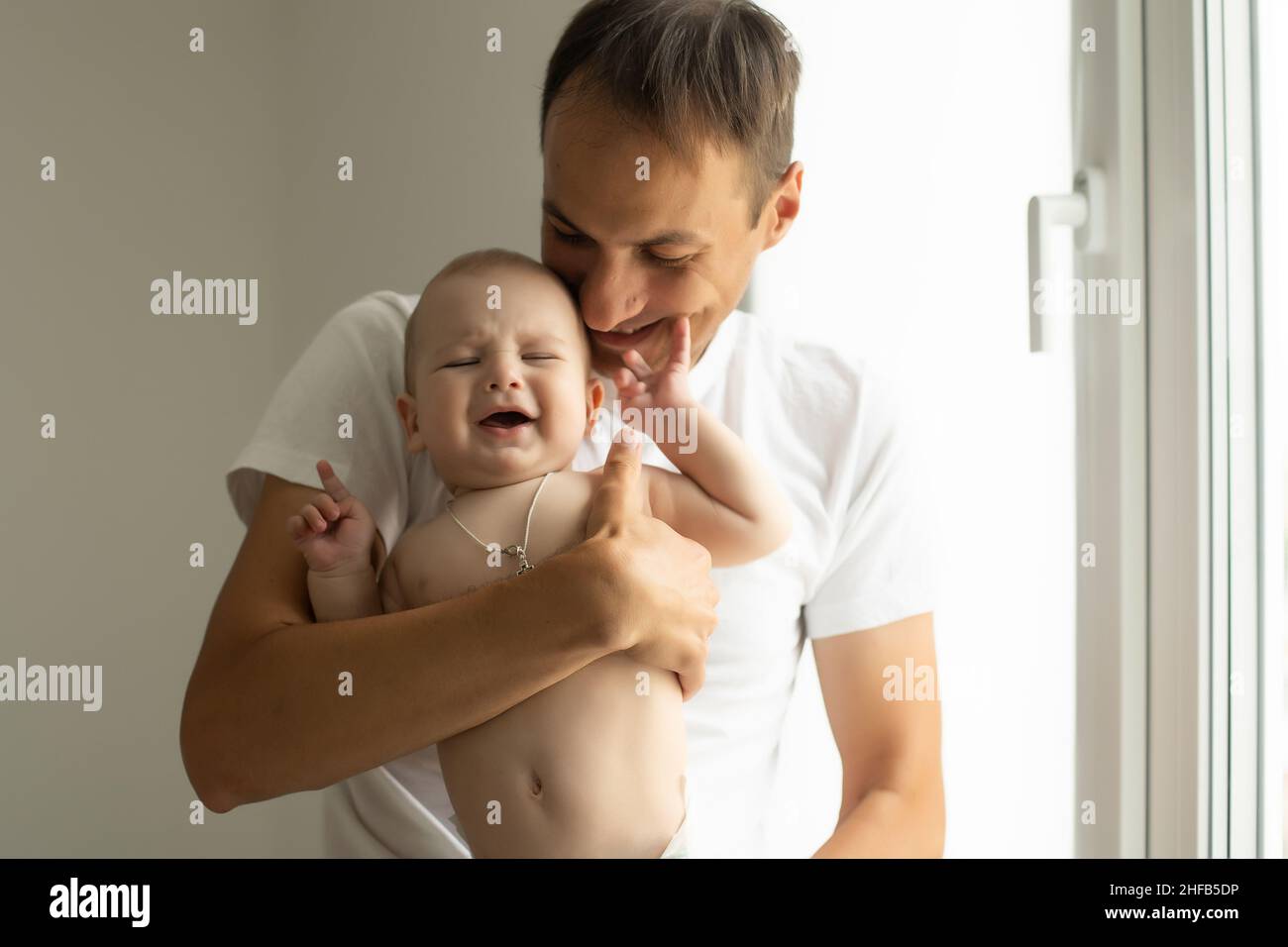 Father Hugging Newborn Baby in white bedroom. Stock Photo