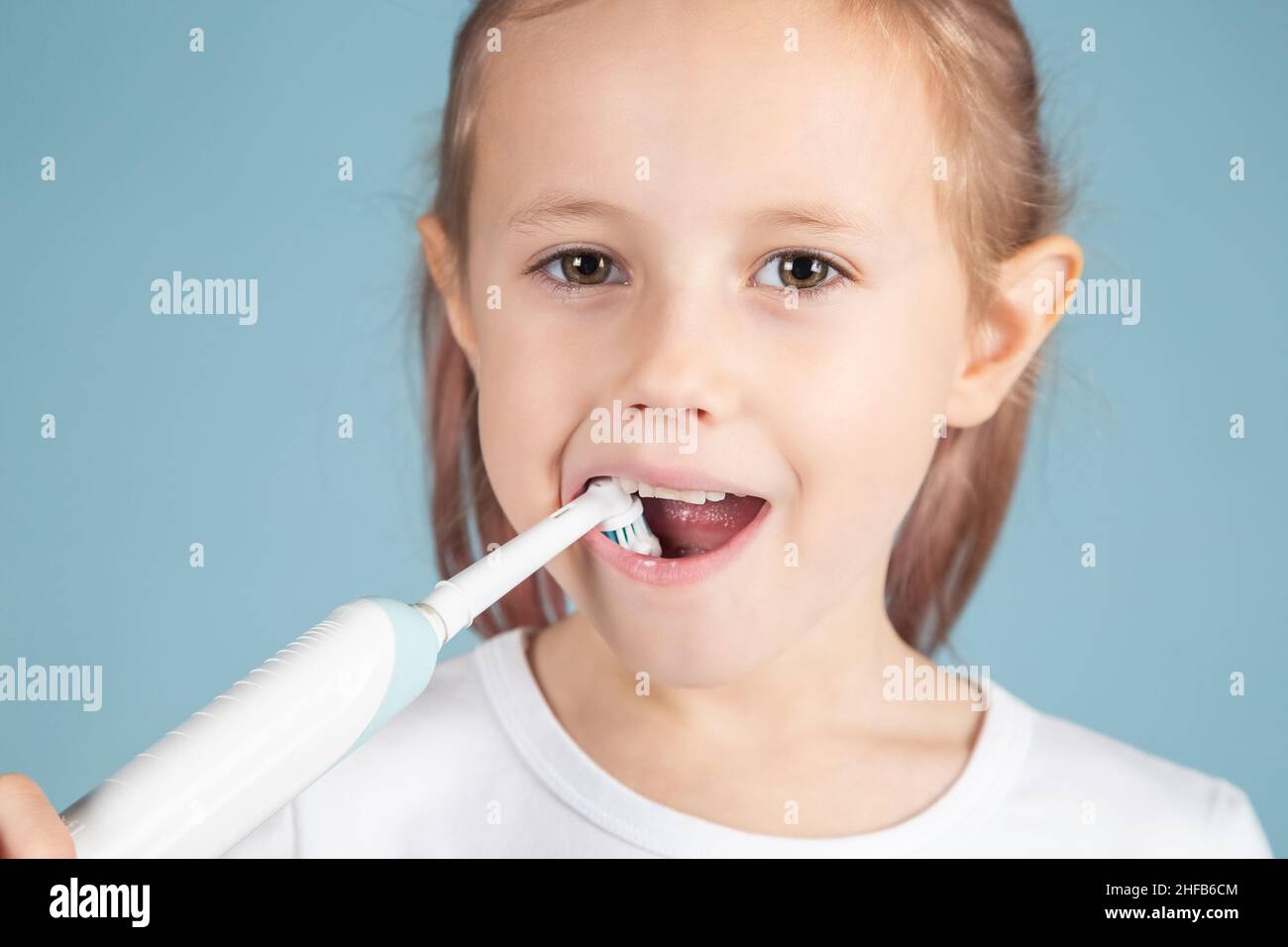 Smiling little caucasian girl brushing teeth Standing Over blue Background, hygiene concept Stock Photo