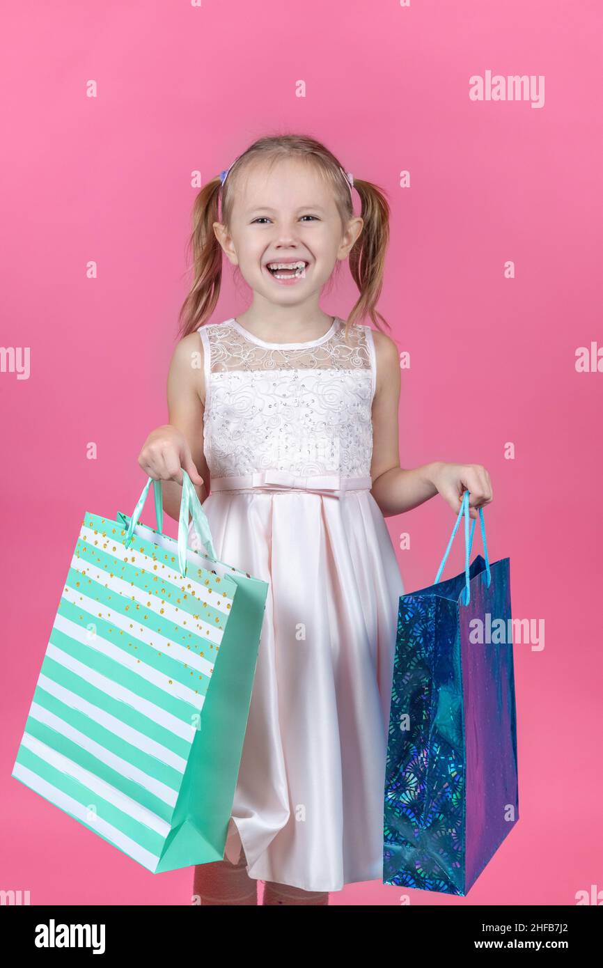 Adorable 6 year caucasian girl holding shopping bags against pink background with copy space. Stock Photo