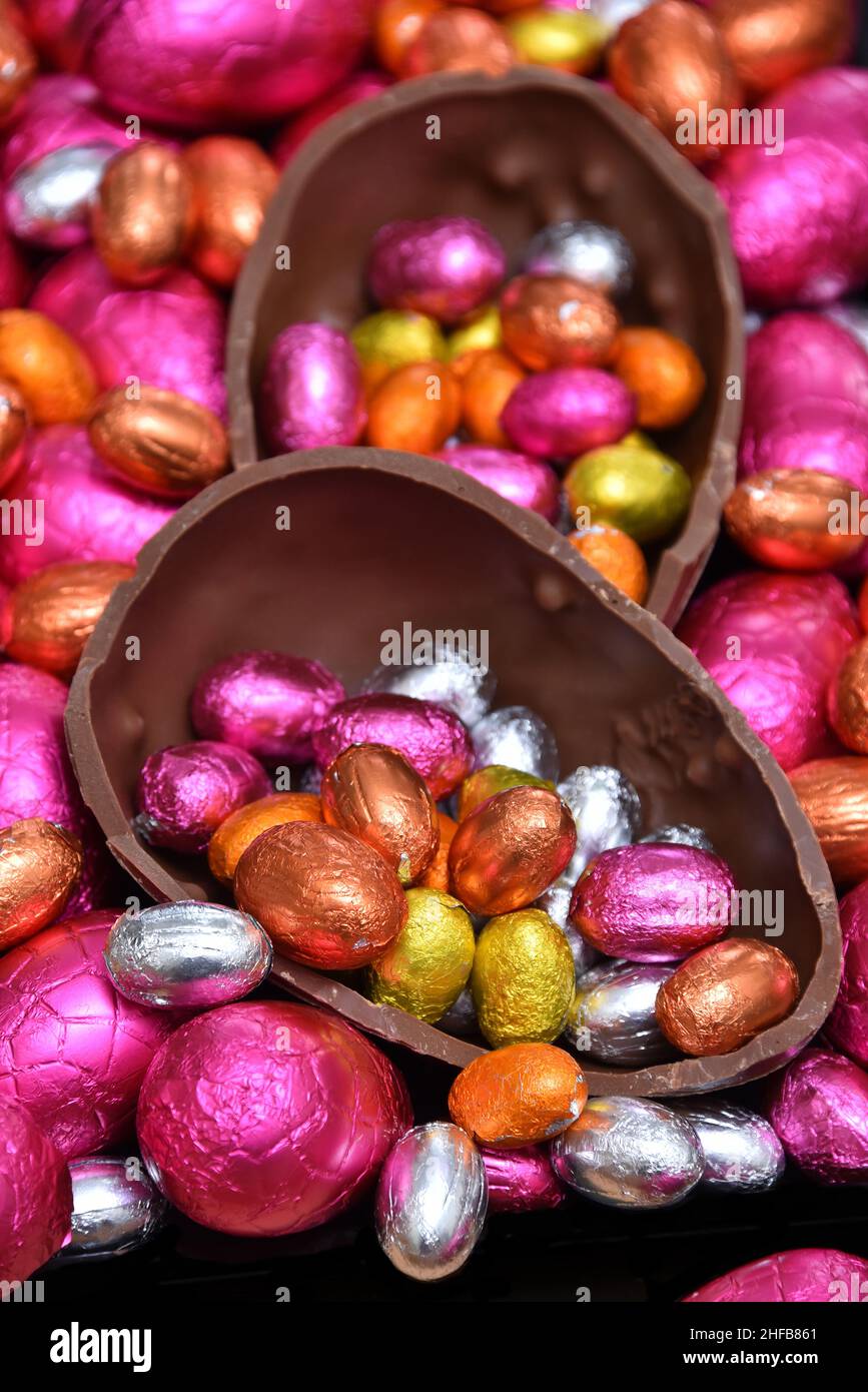 Pile of different sizes of colourful foil wrapped chocolate easter eggs in pink, red, gold, silver and orange with two halves of a chocolate egg. Stock Photo