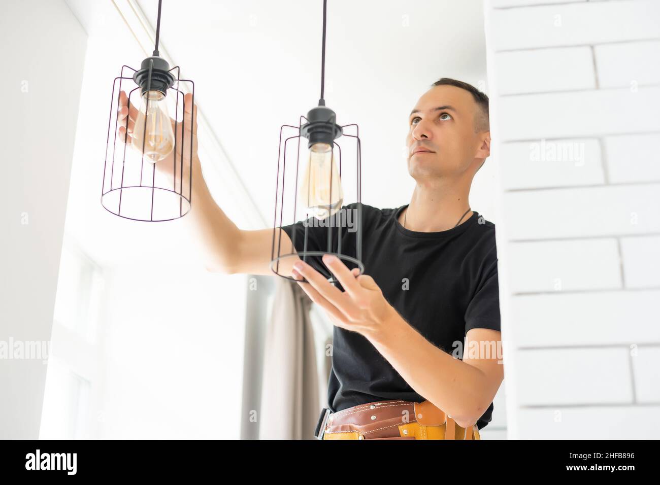 Worker repairing lamp on stretch ceiling indoors Stock Photo