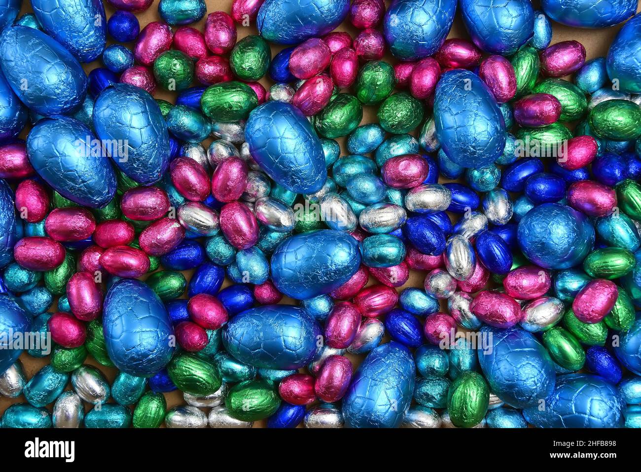 Large & small pink, blue, green and silver foil wrapped chocolate easter eggs, against a pale wood background. Stock Photo