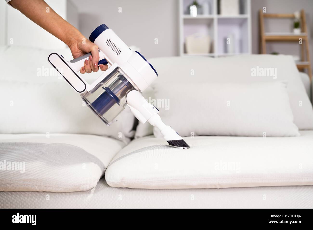Young Female Worker Cleaning Sofa With Vacuum Cleaner Stock Photo