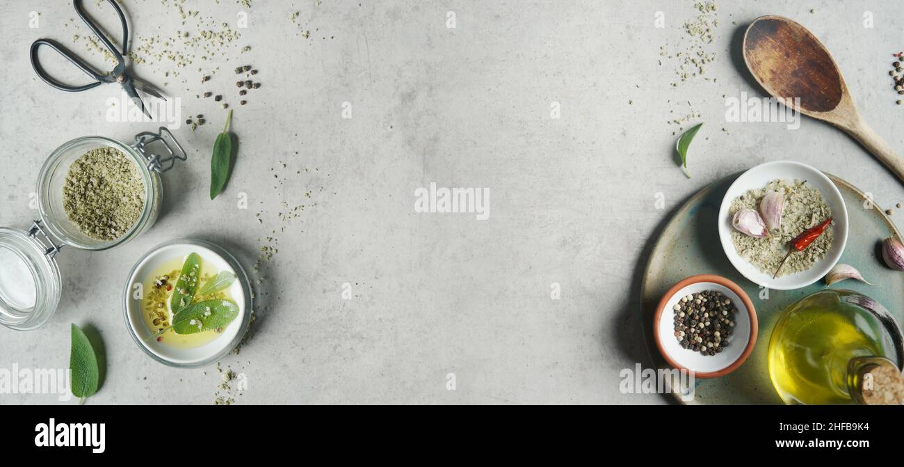 Food background with salt, herbs and spices, wooden cooking spoon, olive oil and kitchen scissors on grey concrete kitchen table. Cooking preparation Stock Photo