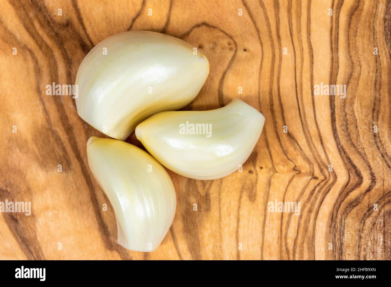 Three garlic cloves over a sandalwood cutting board Stock Photo - Alamy