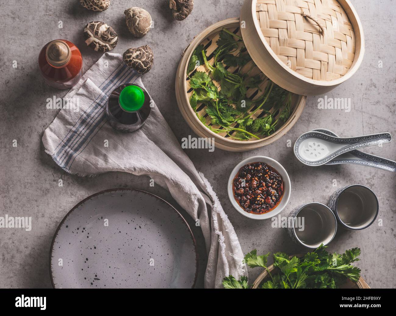 Asian food on grey concrete: shiitake mushrooms, steaming basket, hoisin sauce, coriander and spicy dip, empty plate and traditional crockery. Food ba Stock Photo