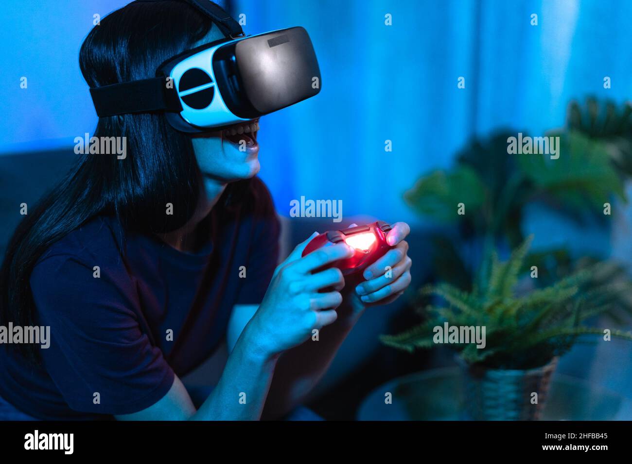 Young woman playing with virtual reality glasses at home - Tech and metaverse concept Stock Photo