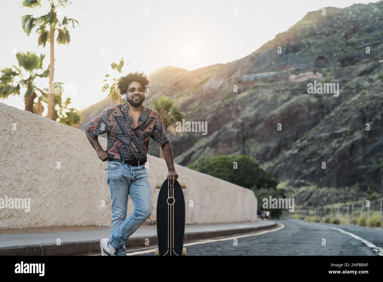 Happy Latin man having fun listening to music and riding on skate during summer time - Youth people lifestyle concept Stock Photo