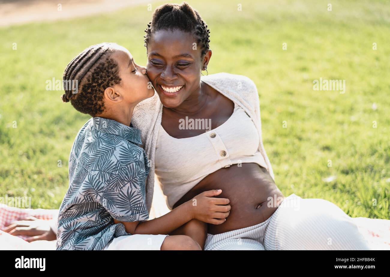 Happy African pregnant mother with son having tender moment in the park - Family love concept Stock Photo