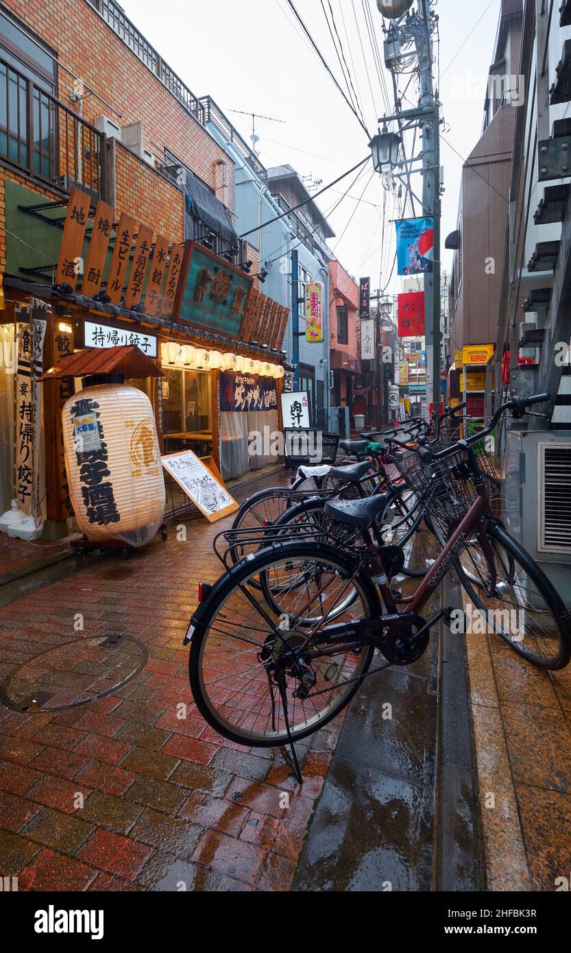 Tokyo, Japan - October 25, 2019: The view of the old market street with bars and restaurants under the heavy rain at twilight. Bicycle is on foregroun Stock Photo