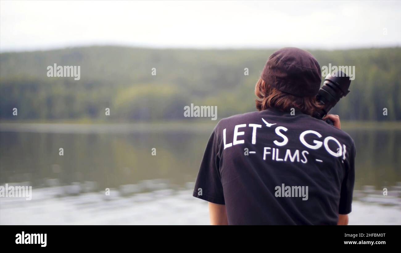 Photographer Back Back view on photographer which looks at lake with a professional ...