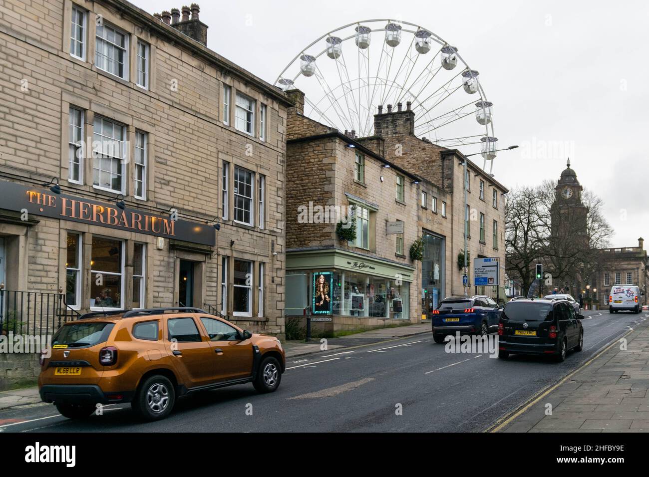 Lancaster, UK - 4th January 2020: A typical English street and road in city centre. Lancaster on Ice Big Wheel in the background with traffic and shop Stock Photo