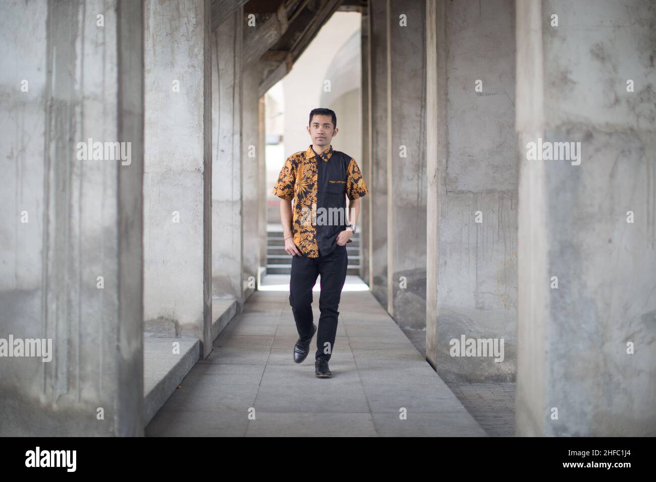 A young male model dressed in Indonesian Batik is posing among rows of pillars at the Long Museum, West Bund, Shanghai China Stock Photo
