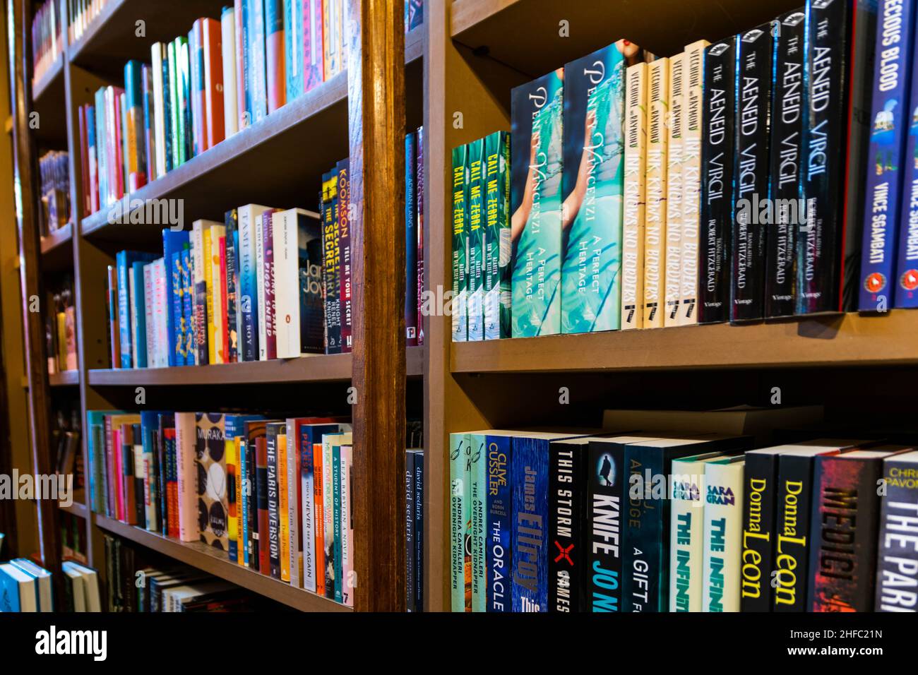 Porto, Portugal - 18 Nov 2020: A variety of books stacked neat and tidy on a wooden book shelf in a book store or library. Organisation concept, Stock Photo