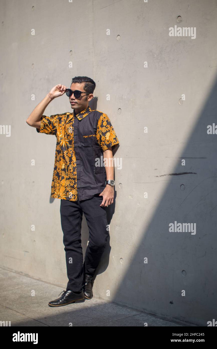 A young male model dressed in Indonesian Batik stands holding sunglasses at the Long Museum, West Bund, Shanghai China Stock Photo