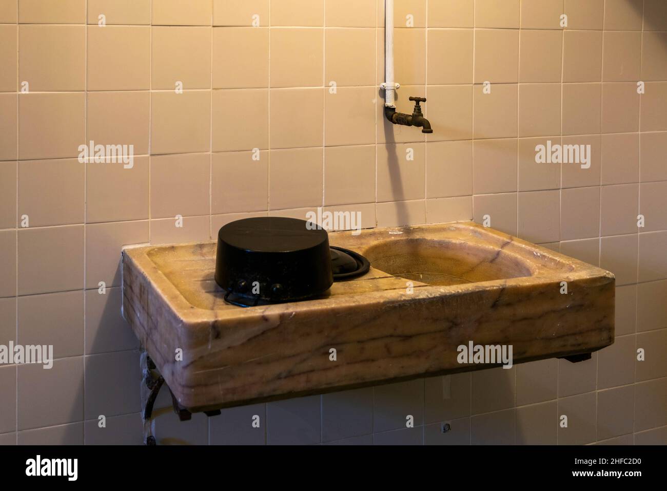 Old wooden limestone sink basin on white tiled wall with rustic tap. Old school 1920s and 1930s bathroom WC. Dirty grunge background. Historic concept Stock Photo