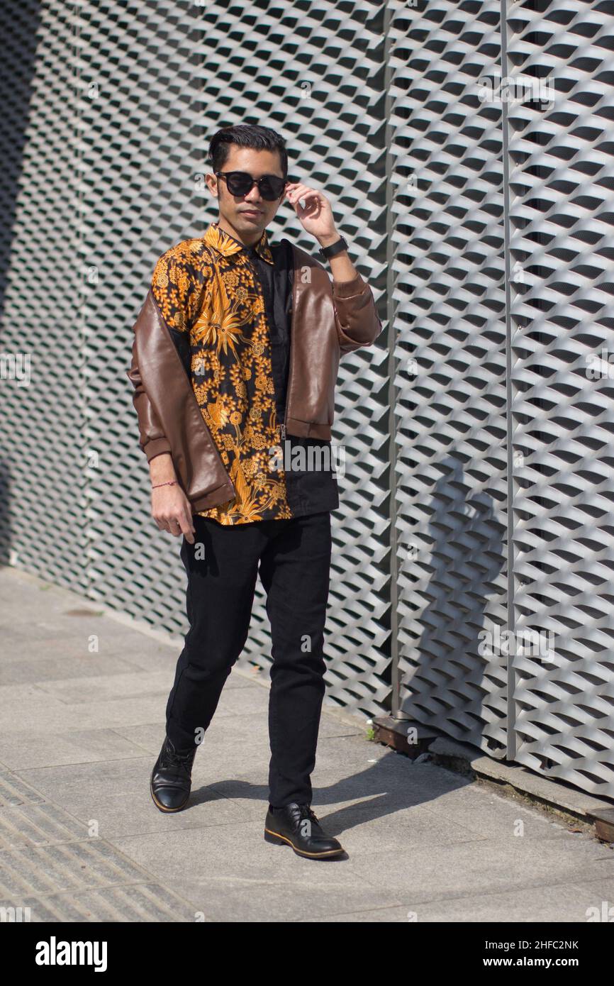 A young male model wearing Indonesian Batik is walking while holding sunglasses at the Long Museum, West Bund, Shanghai China Stock Photo