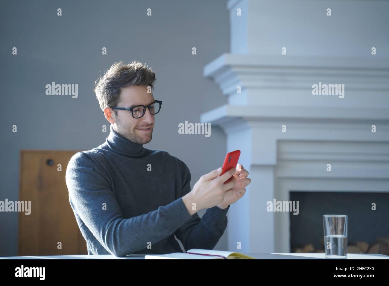 Young handsome german man in glasses sitting at table and using mobile phone at home Stock Photo