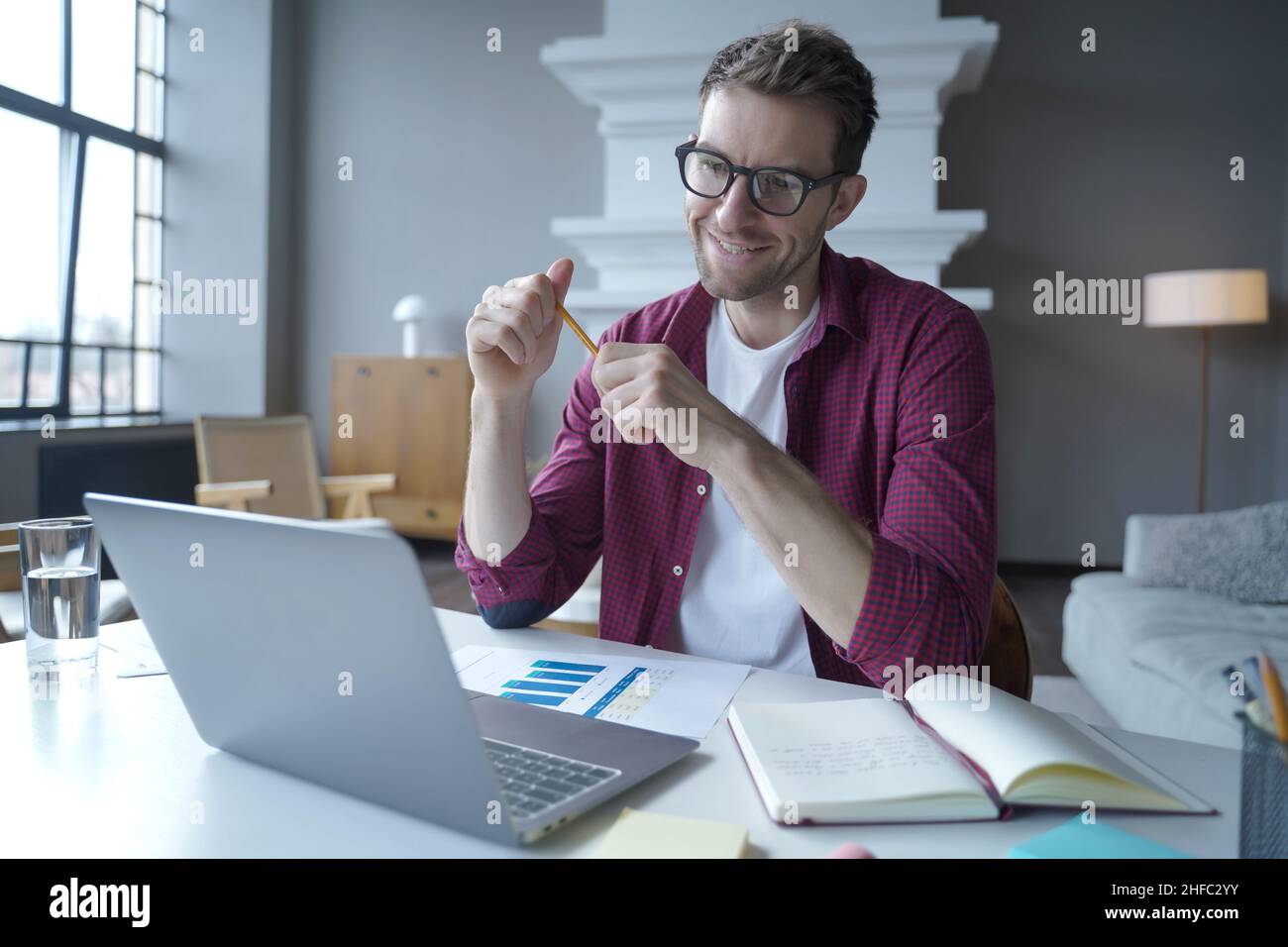 German young male entrepreneur in glasses having pleasant online conversation with colleagues Stock Photo