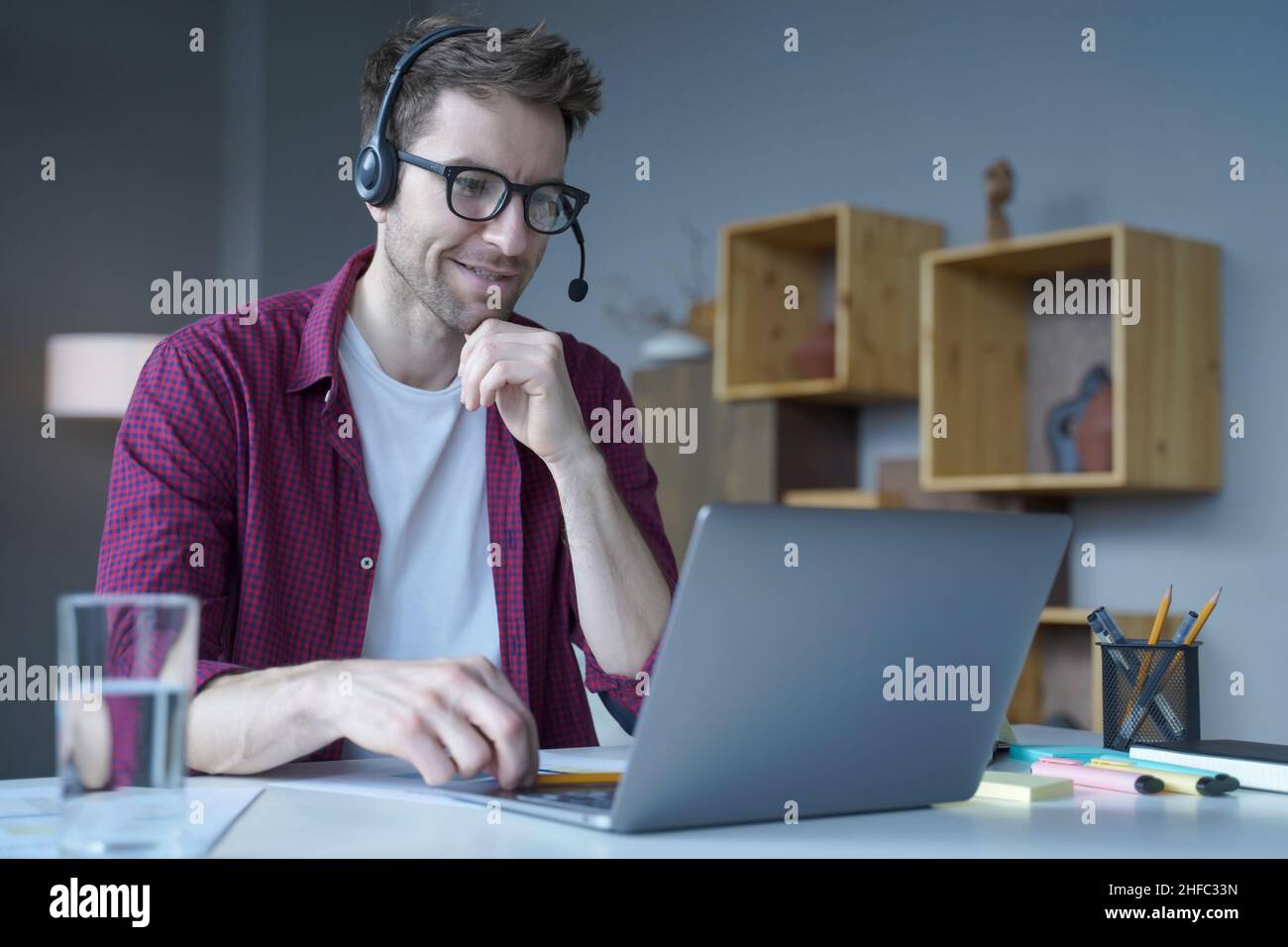 Smiling German guy sitting at home in wireless headset and taking part in online meeting Stock Photo