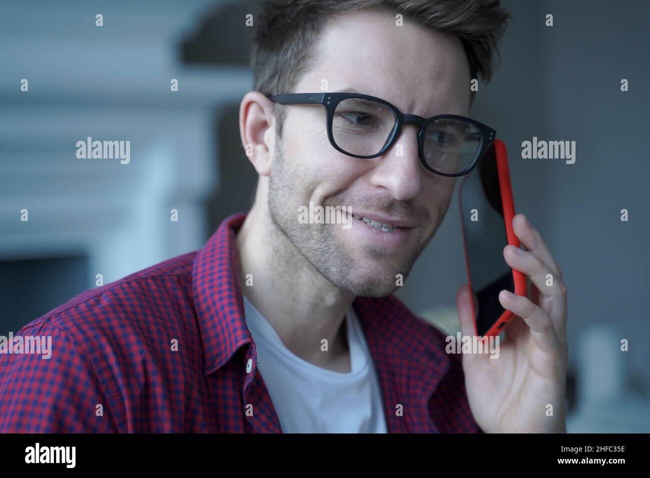 Young smiling german guy in glasses using mobile phone and talking on with friend Stock Photo