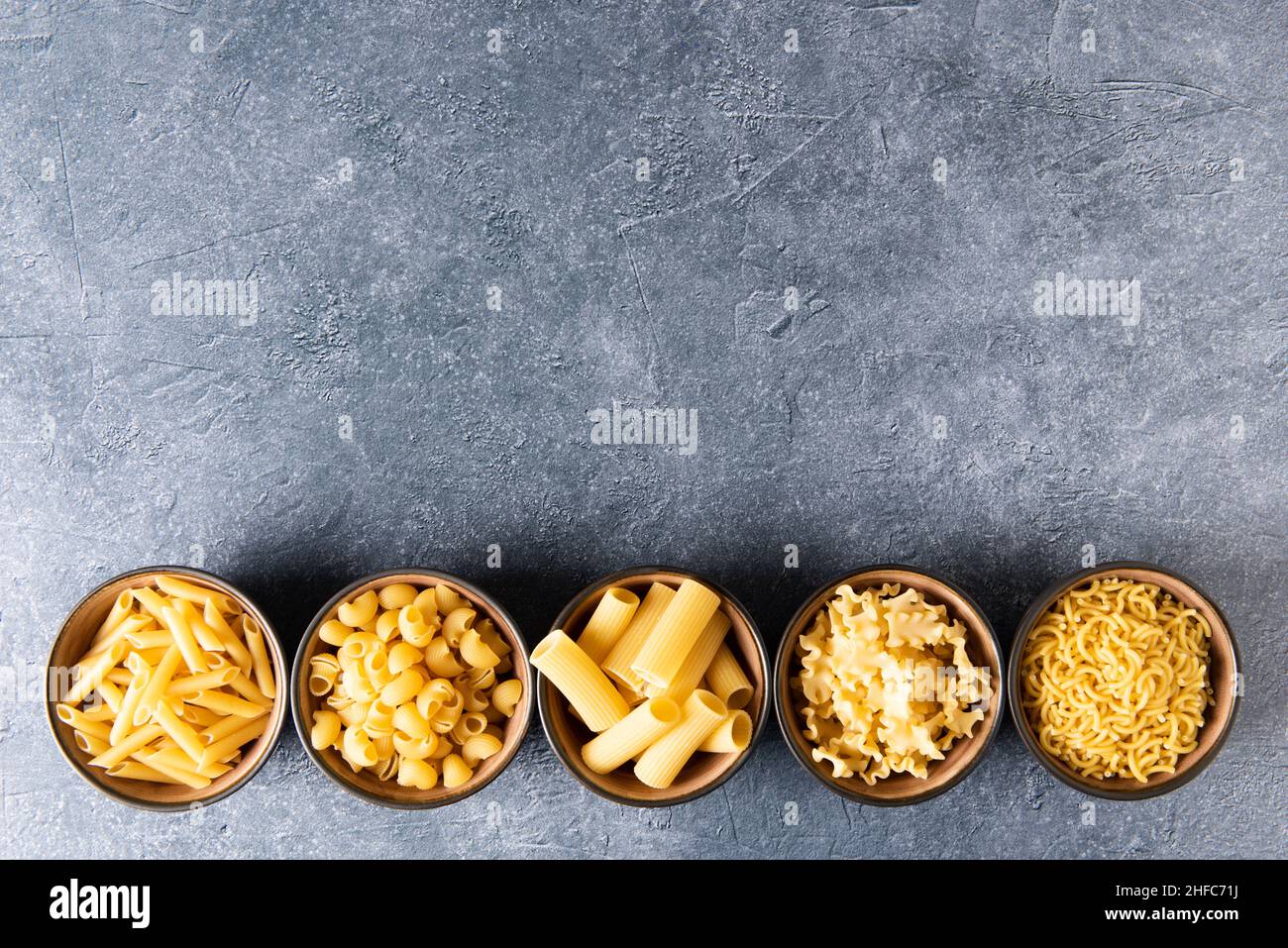Variety of pasta in bowls with copy space above, in stone background. Stock Photo