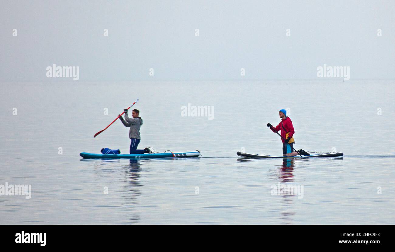 Portobello, Edinburgh, Scotland, UK. 15th January 2022.  Calm Firth of Forth for another cloudy afternoon, temperature of 7 degrees centigrade for those engaged in watersports. Pictured: Two males on paddleboards enjoy the calm conditions. Credit: Archwhite/Alamy Live News. Stock Photo