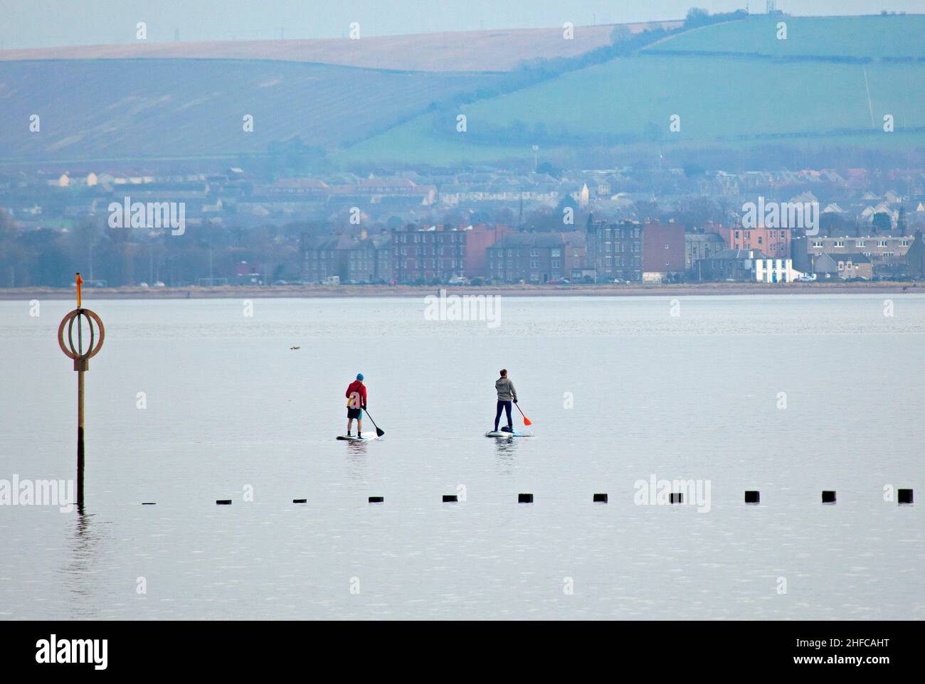 Portobello, Edinburgh, Scotland, UK. 15th January 2022.  Calm Firth of Forth for another cloudy afternoon, temperature of 7 degrees centigrade for those engaged in watersports. Pictured: Two males on paddleboards enjoy the calm conditions with East Lothian in the background. Credit: Archwhite/Alamy Live News. Stock Photo