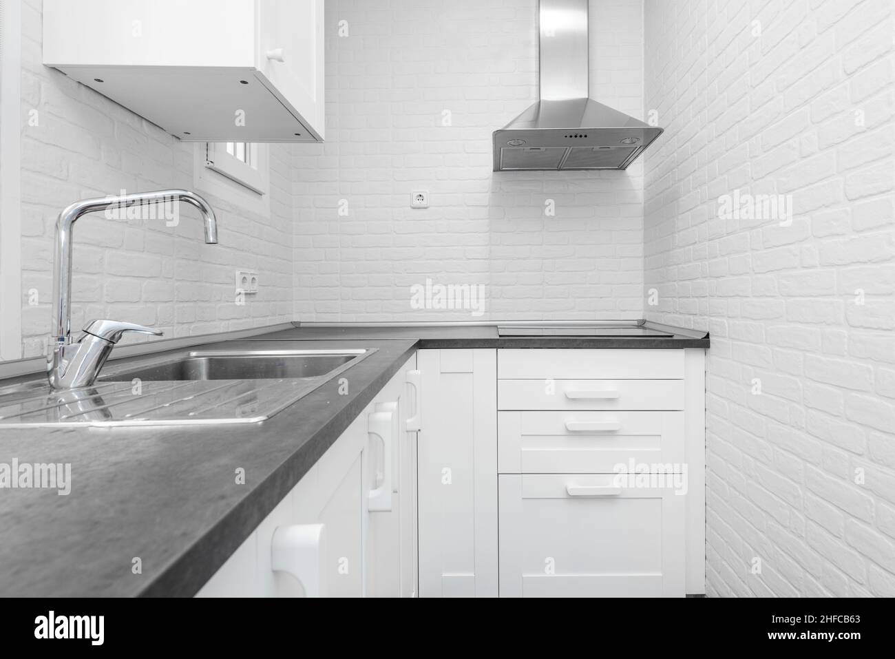 Vacation rental kitchen with white cabinets, white brick walls, gray countertop and stainless steel sink and range hood in the corner Stock Photo