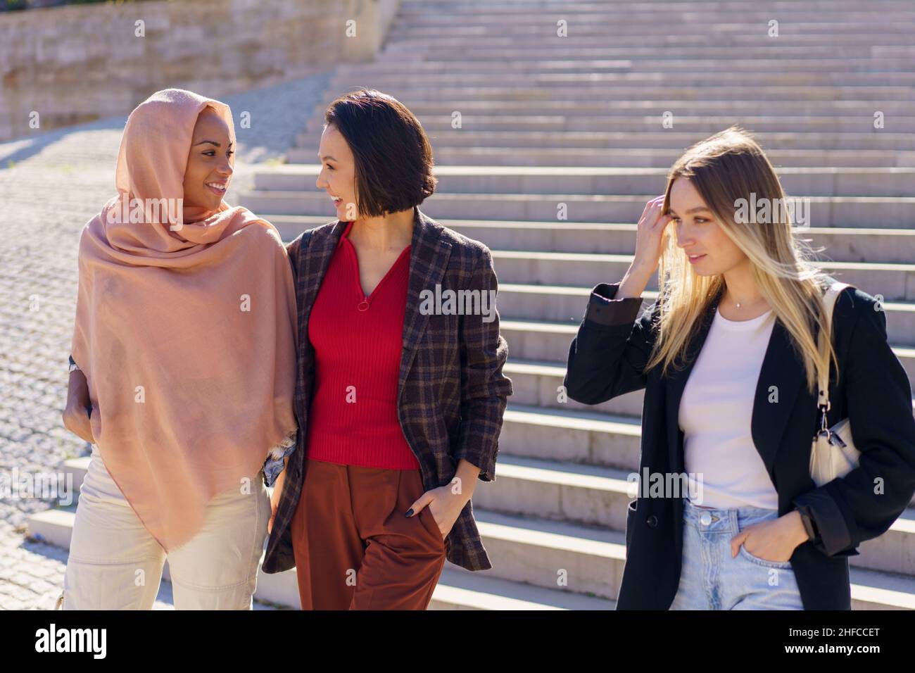 Positive young diverse female friends walking downstairs in campus Stock Photo