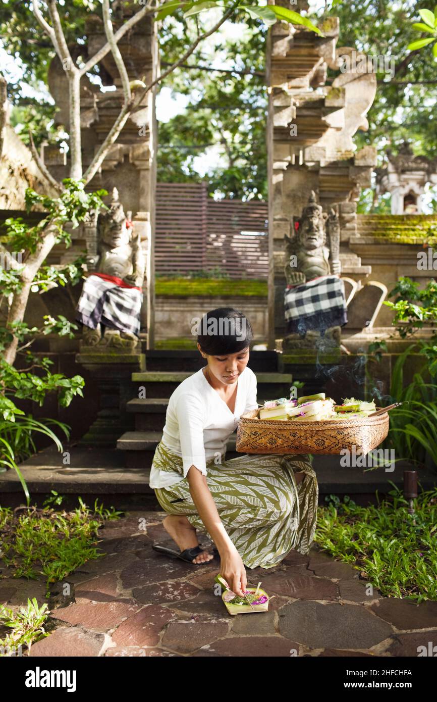 Balinese woman makes morning offerings at Kayumanis Gangsa, Bali, Indonesia. These offerings to the spirits are made on a daily basis throughout Bali. Stock Photo