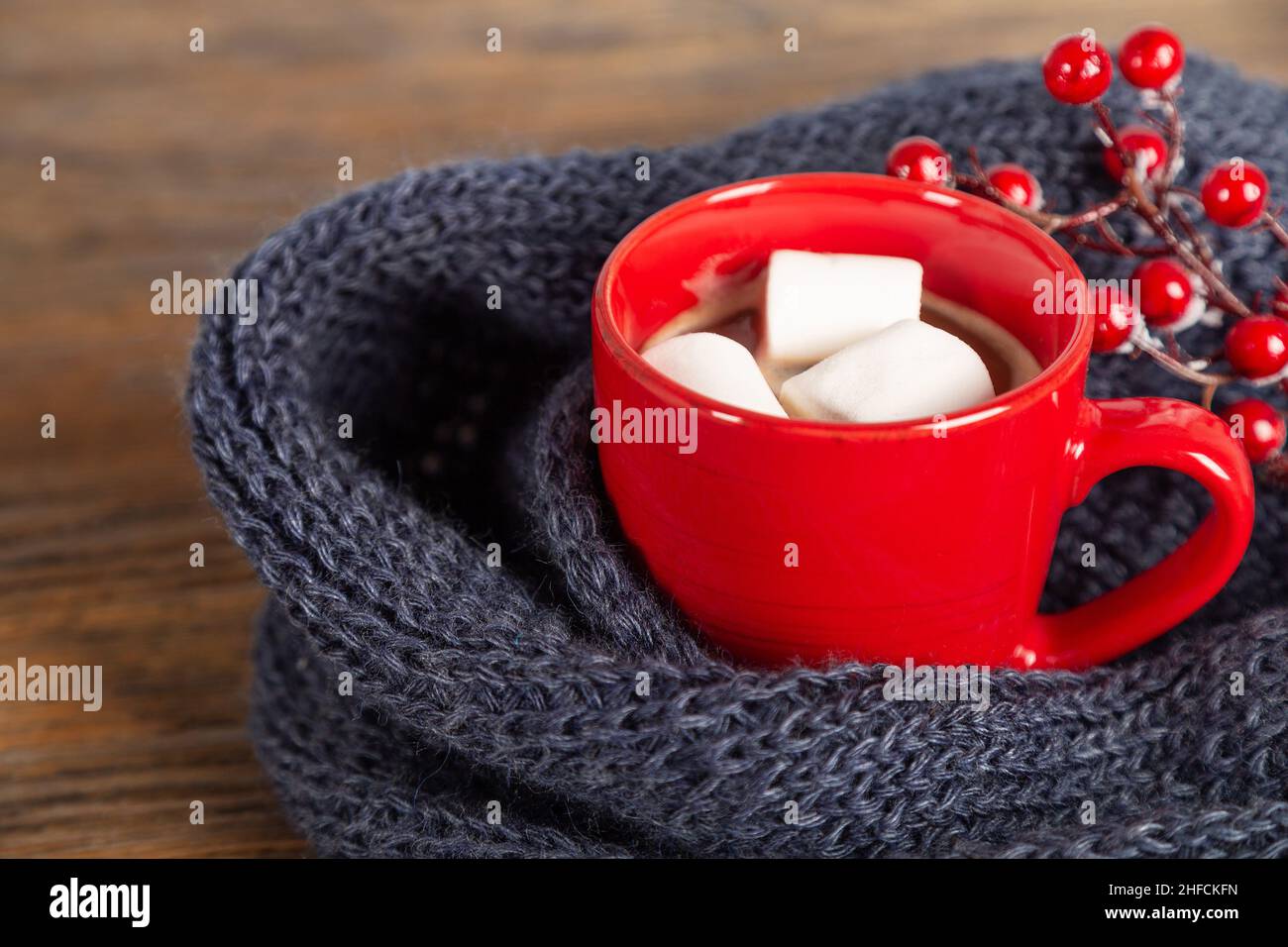 Christmas and winter cozy background with knitted scarf and red mug with cocoa or hot chocolate. Stock Photo