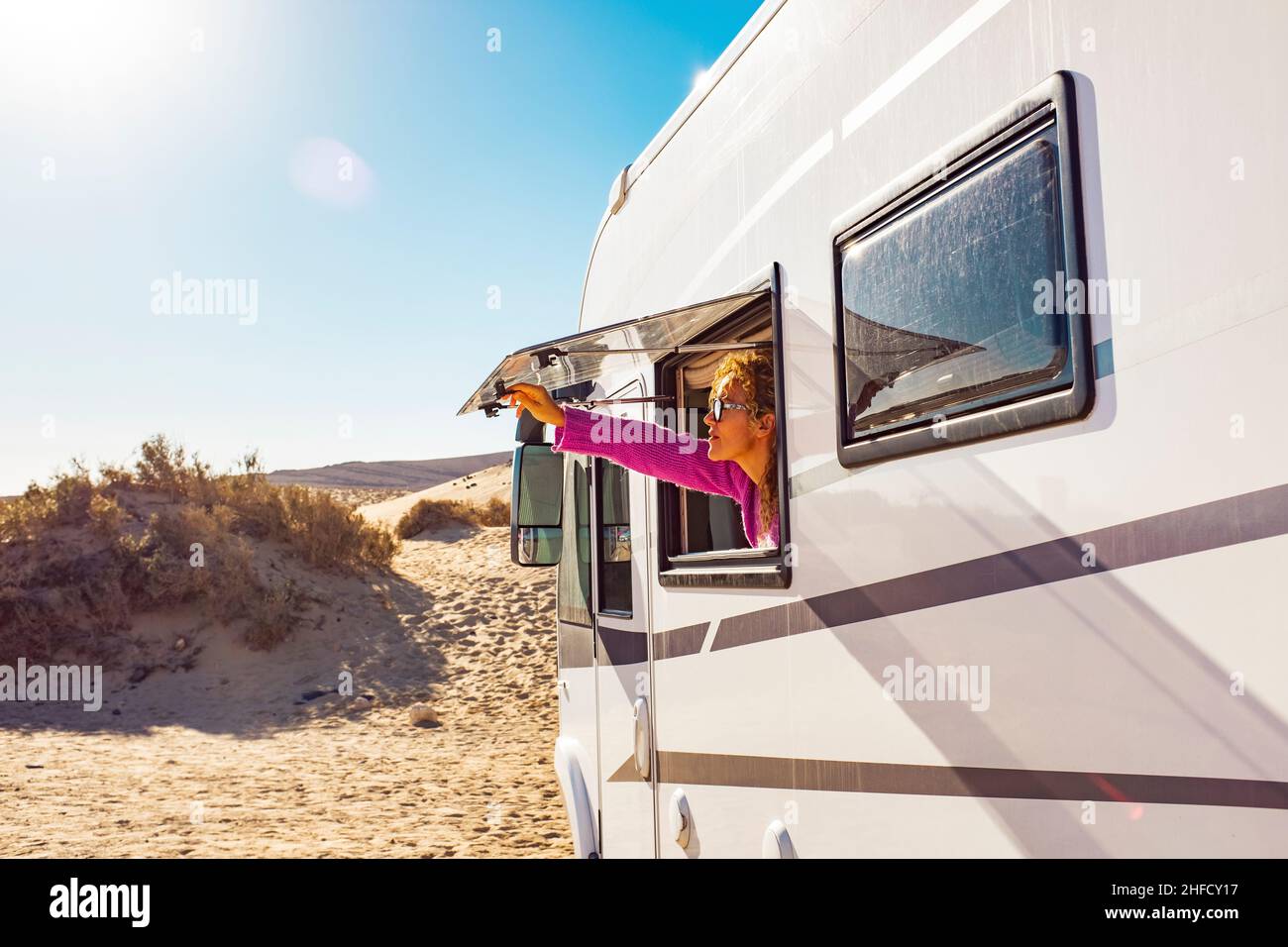 Adult tourist woman opening camper van window to enjoy the sun and freedom. Concept of travel people for summer holiday vacation inside camping car mo Stock Photo