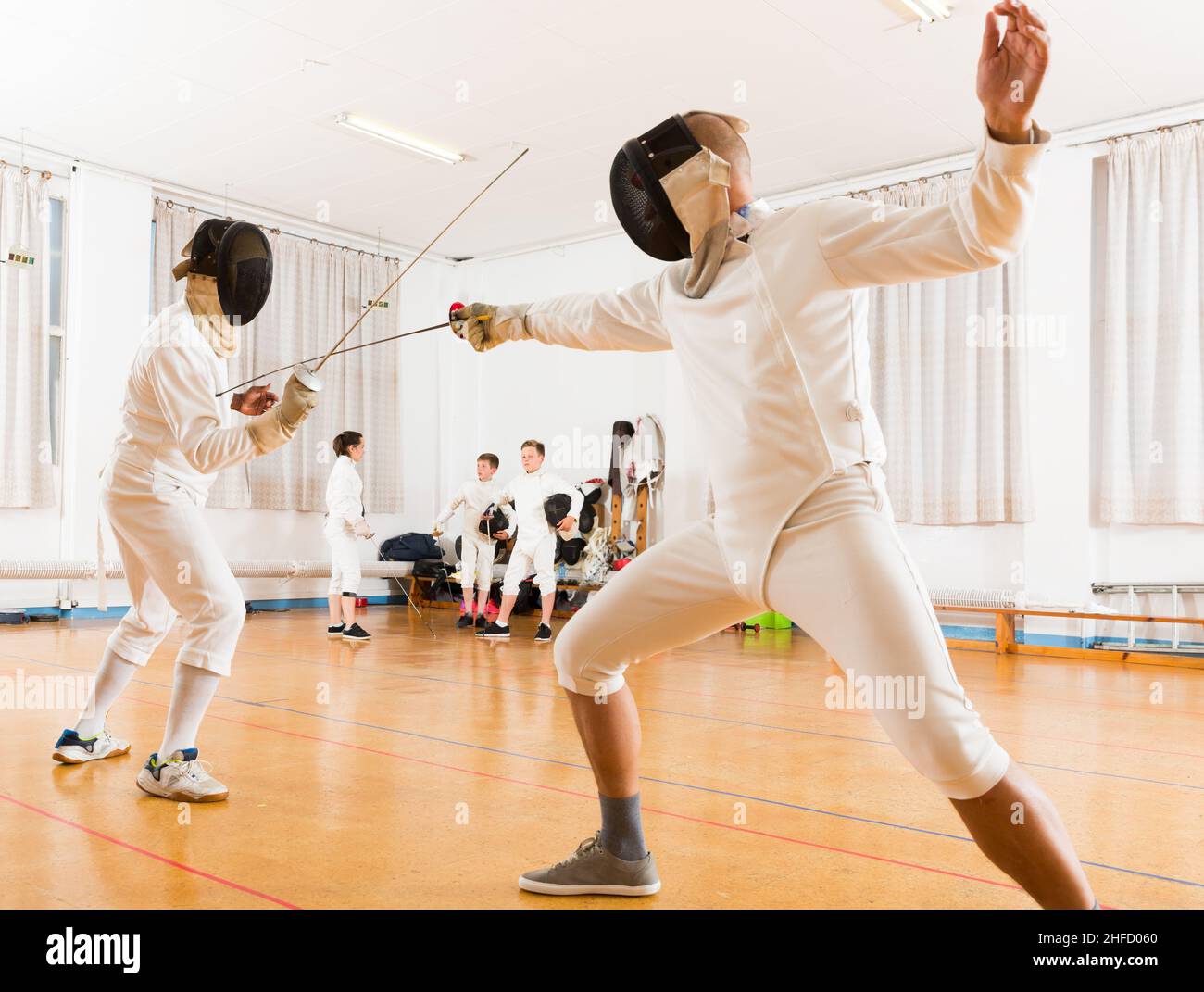 Adults and teens wearing fencing uniform practicing with foil Stock