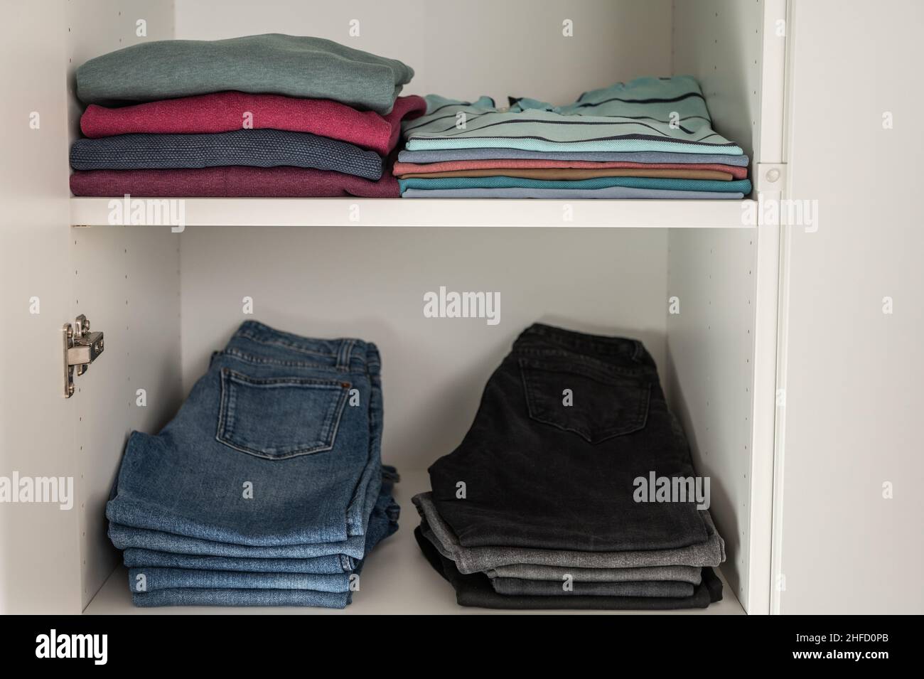 Neatly folded sweaters and jeans and other clothes on shelves in wardrobe Stock Photo