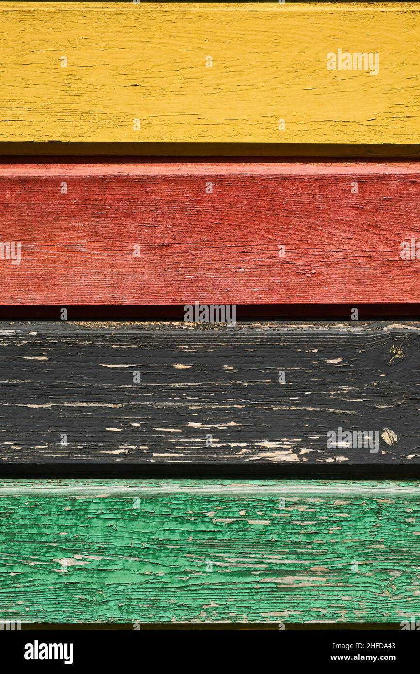 Background of multi colored rough boards, yellow, red, black, and green. Peeling paint wood texture with old faded colors. Rustic wooden pattern wall. Stock Photo