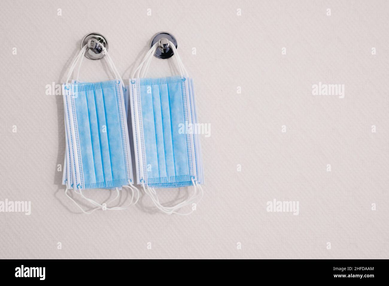 Blue face masks hanging on the white wall background. Concept of coronavirus pandemic. Copy space for the text. Stock Photo