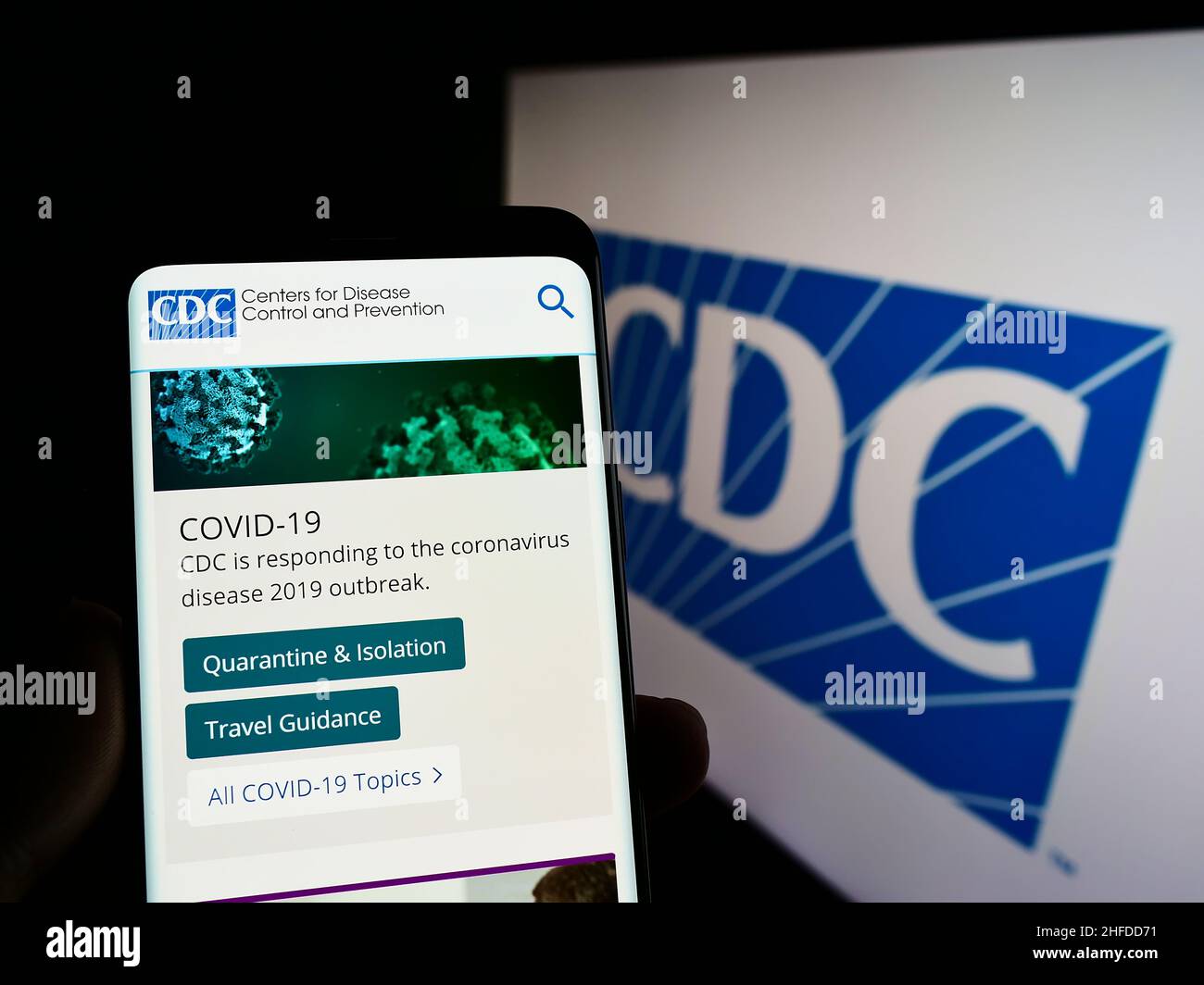 Person holding smartphone with website of Centers for Disease Control and Prevention (CDC) on screen with logo. Focus on center of phone display. Stock Photo