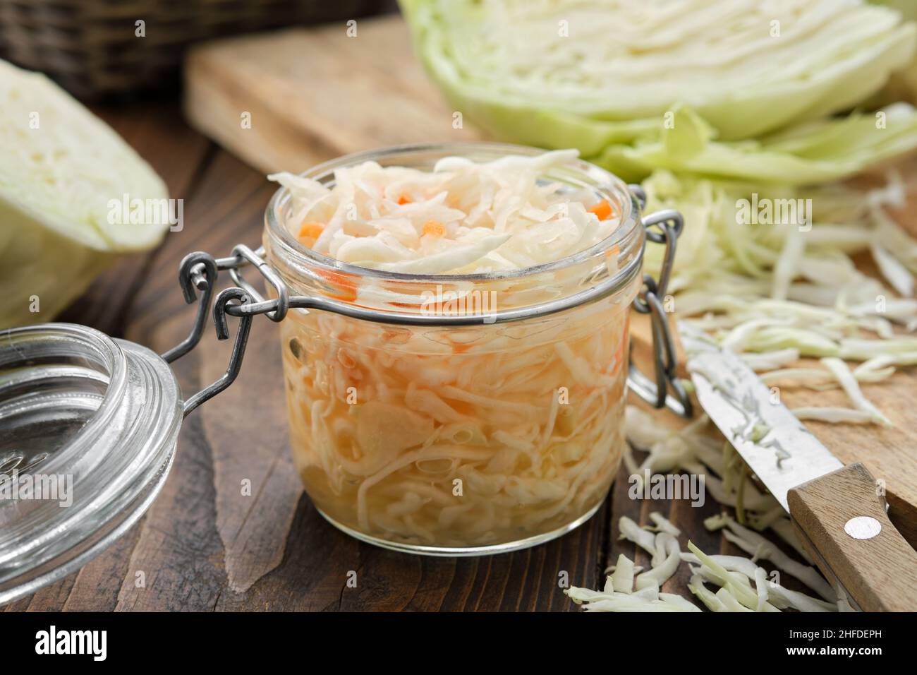 Jar of sour cabbage, pickled sauerkraut. Fermented cabbage, coleslaw salad. Chopped cabbage on a cutting board for making sauerkraut on background. He Stock Photo