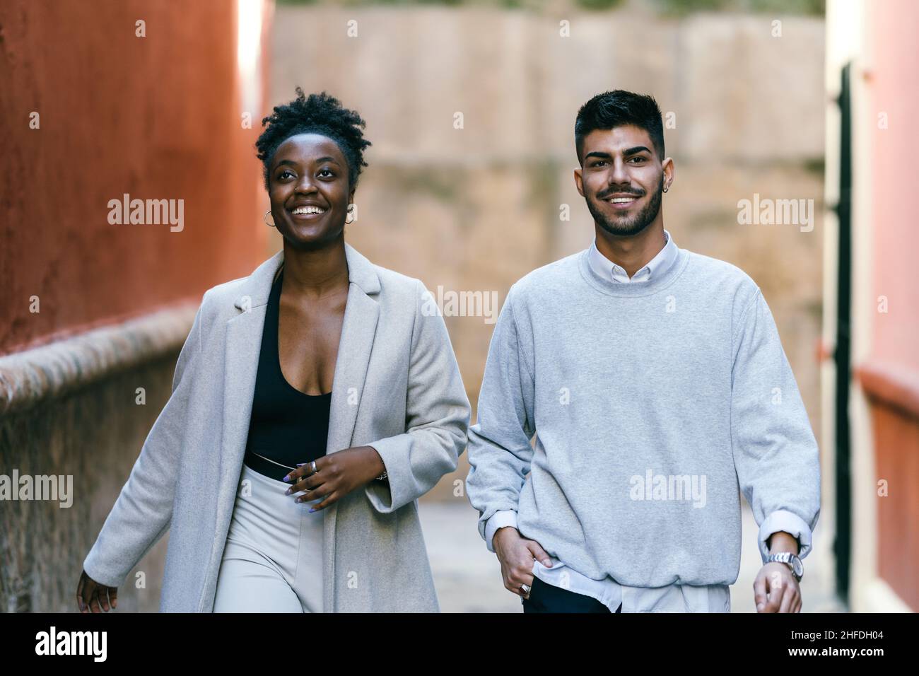 Two smiling models of different ethnicities walking through a narrow street Stock Photo
