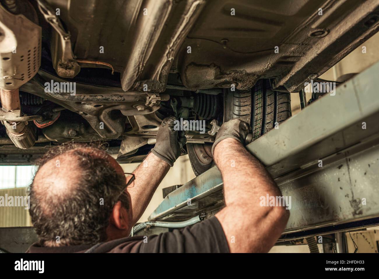 Back of a man under a car fixing steering alignment in a garage Stock ...